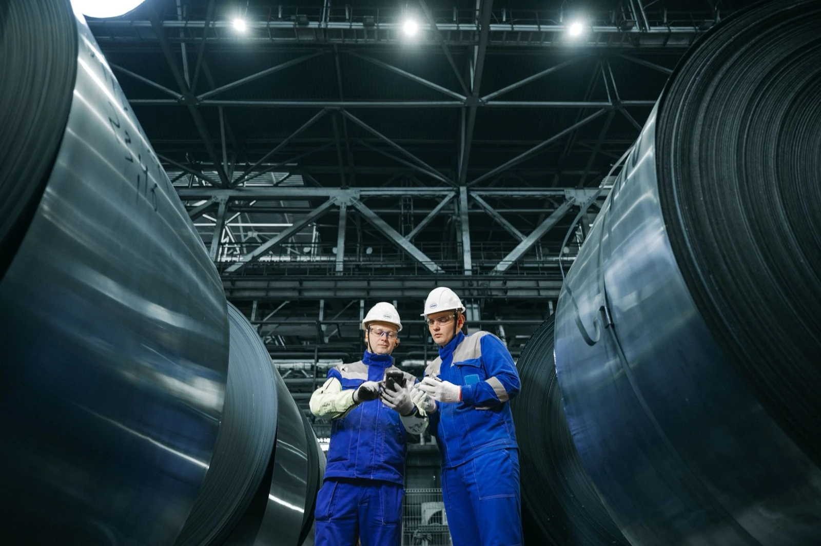Twee medewerkers met helm controleren staalrollen in een fabriekshal