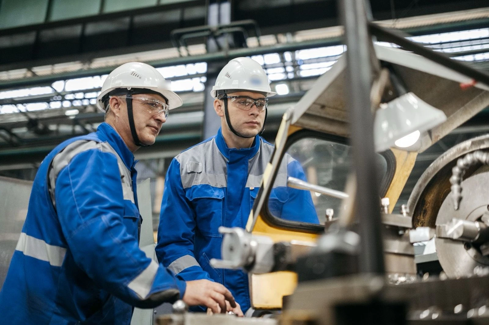 Twee monteurs met helm aan een draaibank in een productiehal